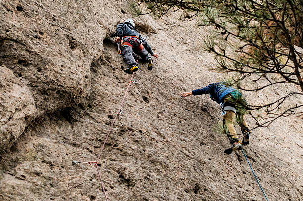 Professional mountaineers in vivid high-altitude gear ascend steep, snow-laden High Mountain terrain. Their determined spirits are evident as they tackle the challenging climb amidst harsh winter conditions, showcasing their resilience and focus in this extreme environment.