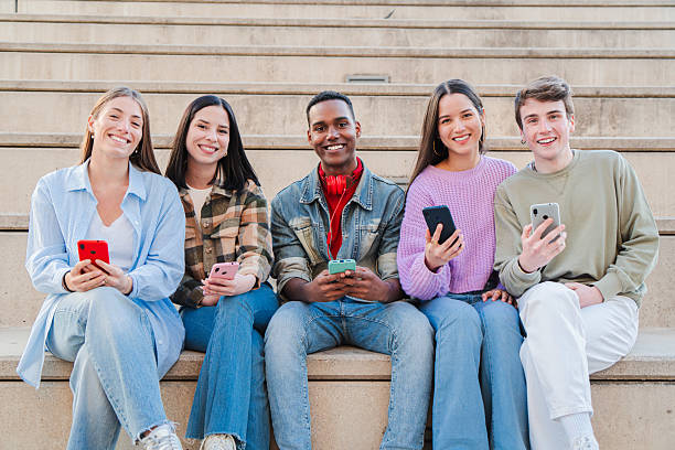 istock Five joyful young friends engaged with their smartphones while sitting together on steps in a lively setting 2229755580