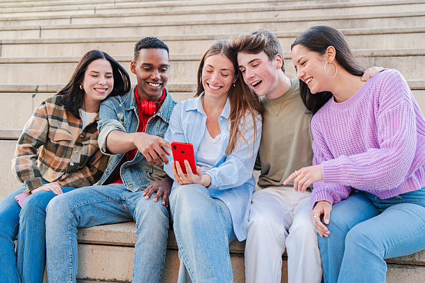 istock Excited group of friends joyfully watching something on a smartphone while sitting together outdoors 2229756173