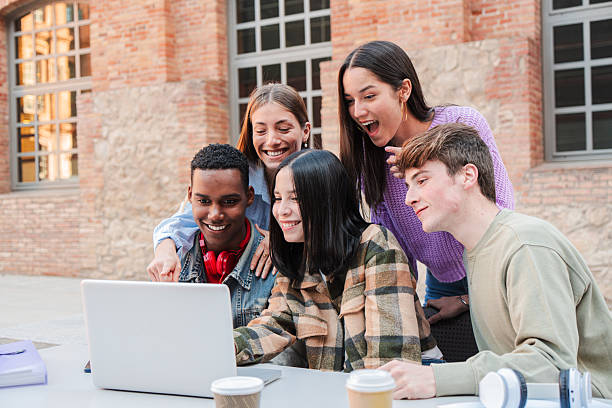 istock Group of enthusiastic students gathered around a laptop, engaged in collaborative study session, sharing ideas and excitement, representing teamwork and learning among teenagers at university campus 2229758783