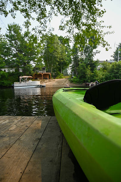 Close up on front of kayak standing on pier on a river during a summer day vacations heatwave. A out of focus man is in the river in background.
