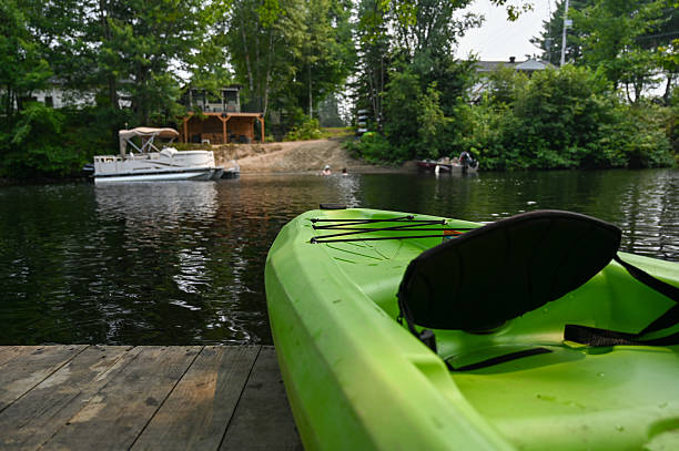 Close up on front of kayak standing on pier on a river during a summer day vacations heatwave. A out of focus man is in the river in background.