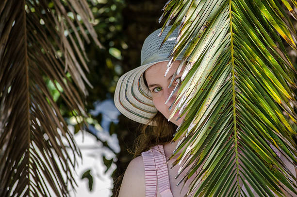 istock Young woman peeking through palm fronds 2229760306