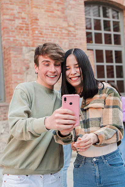 istock Vertical. Two student people having fun with a mobile phone outdoors. Young friends browsing on internet with a cellphone. Teenagers sharing photos on the social media using a smartphone application 2229760612