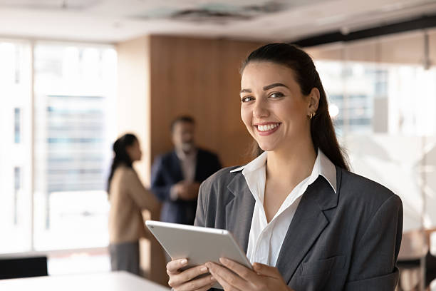 istock Cheerful millennial businesswoman looking at camera with pad in hands 2229763538