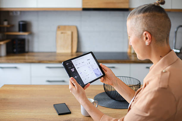 istock Woman using a touchscreen device to manage smart home functions from the comfort of the kitchen 2229763648