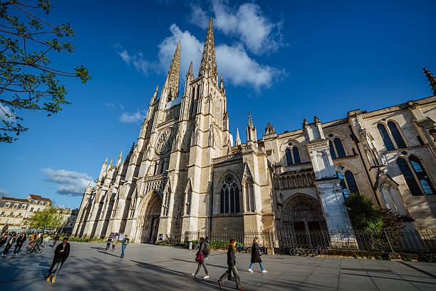 A majestic Gothic-style cathedral in Bordeaux, France, with notable architecture and bustling pedestrians under a clear blue sky.