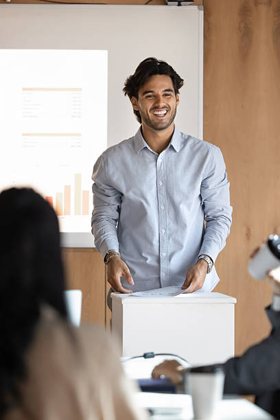 istock Smiling millennial man business presenter stand at lectern hold speech 2229766177