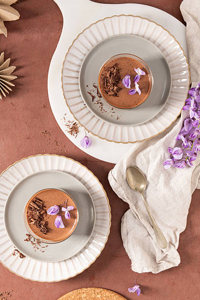 istock An overhead view showcases two creamy chocolate mousses in glasses, elegantly styled on plates with flowers and other decorative elements on a rustic surface. 2229768042