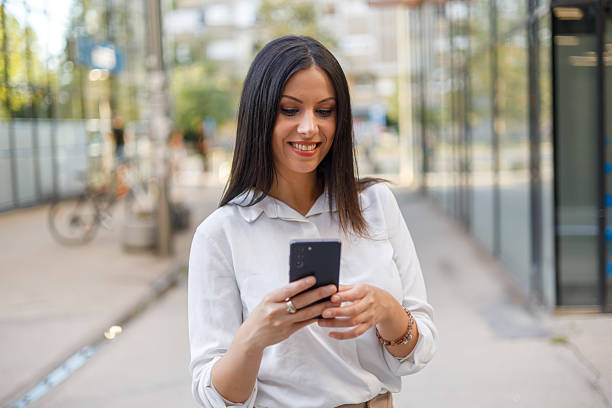 istock Professional businesswoman scrolling smartphone while walking urban sidewalk, embodying connectivity amid city energy 2229770949