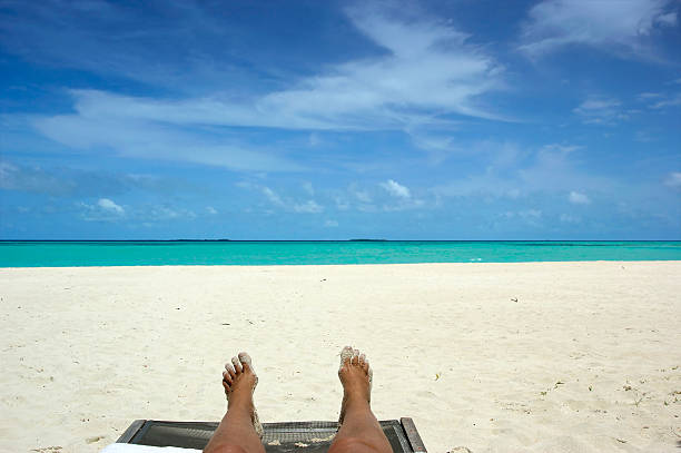 Sandy feet of a woman on a sun lounger above tropical beach with view over ocean