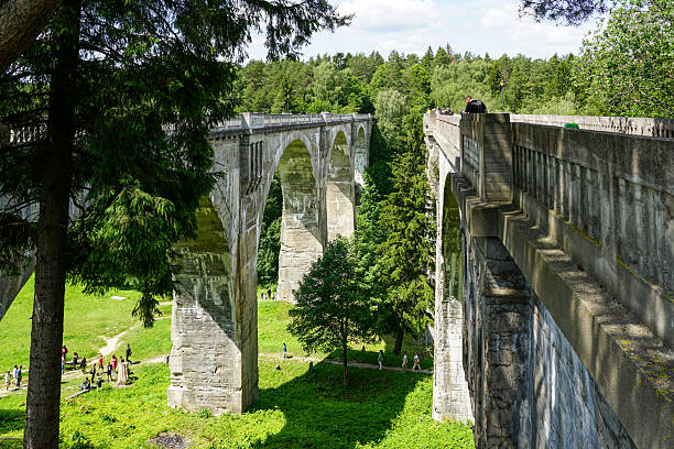 Stanczyki, Poland- June 21, 2025: Historic Stanczyki stone arch bridge, framed by green trees, tourists walking and enjoying the scenic view.