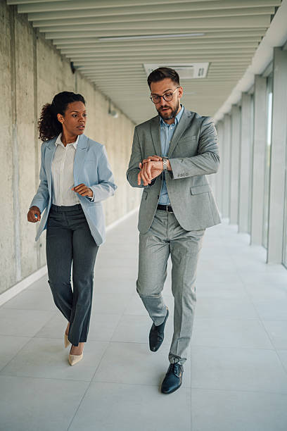 istock Businessman checking time while walking in office hallway with colleague 2229782947