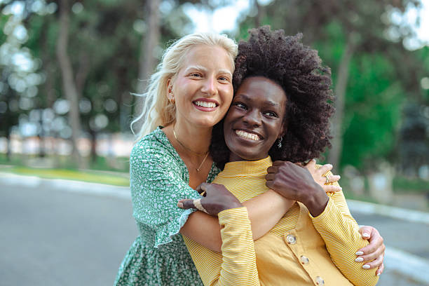 istock Two diverse friends hugging and smiling at the park on a sunny day 2229785597