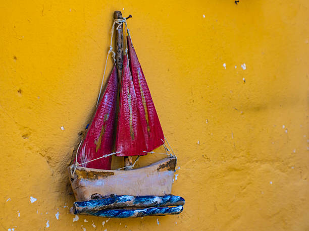Small boat with red sails, a Greek souvenir hanging on a yellow wall, Greece