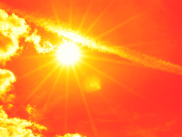 Bright sun with beautiful beams in the sky with some clouds. Toned in red color, space for copy.