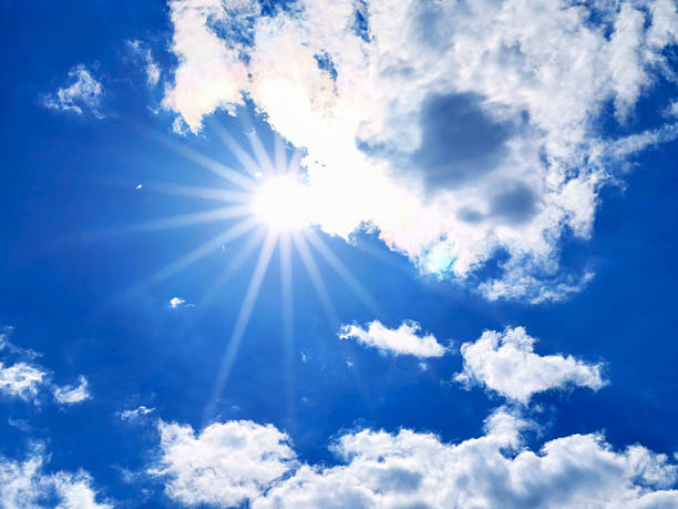 A vibrant display of sunlight bursts through a blue sky, creating radiant beams. Wispy clouds add texture to the atmosphere on a beautiful summer day. Space for copy.