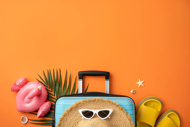 istock Vibrant summer items arranged with a suitcase, hat, and travel accessories on orange background 2229790842