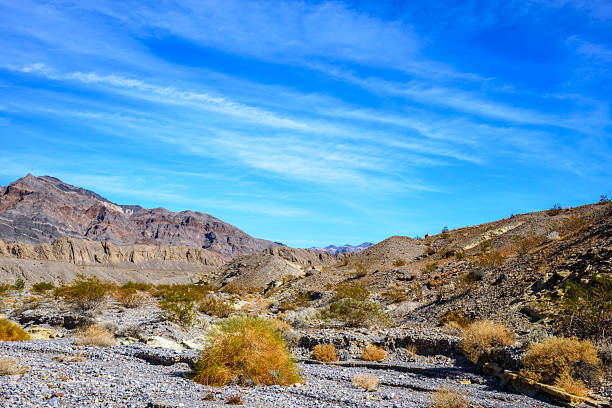 Looking across the entrance to Hole in the Wall Canyon, layers of golden sedimentary rock rise against the rugged peaks beyond. Shaped by ancient seas, earthquakes, and floods, this wild landscape reveals the raw geological history that makes Death Valley so extraordinary.  Hole in the Wall Canyon is in Death Valley National Park near Furnace Creek, California, USA.