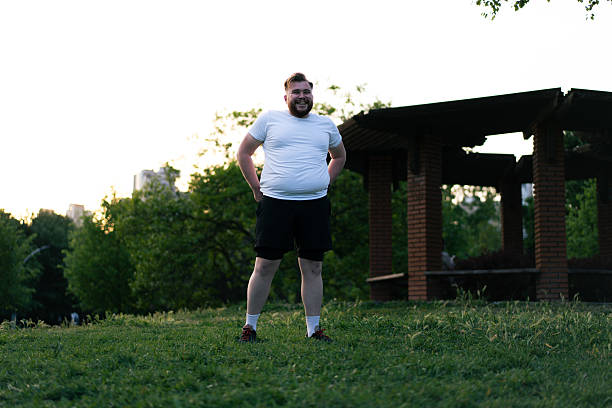 Young man with overweight problems is smiling and exercising in a city park
