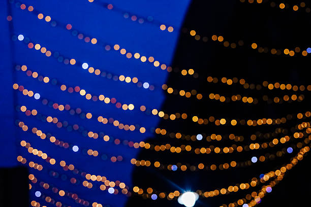 Warm yellow lights hang across a winter evening sky enhancing the cheerful ambiance of the city square bustling with people.