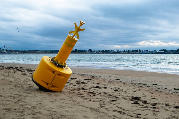 Yellow buoy on sandy beach with overcast sky near ocean shore.