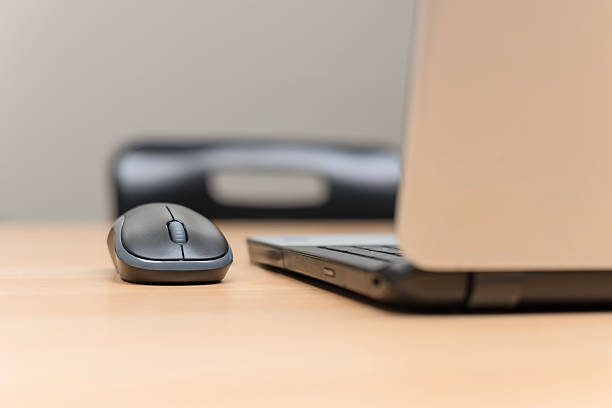 Open laptop and wireless computer mouse on a wooden conference table, with a black office chair in the background, symbolizing modern workplace technology and business meetings