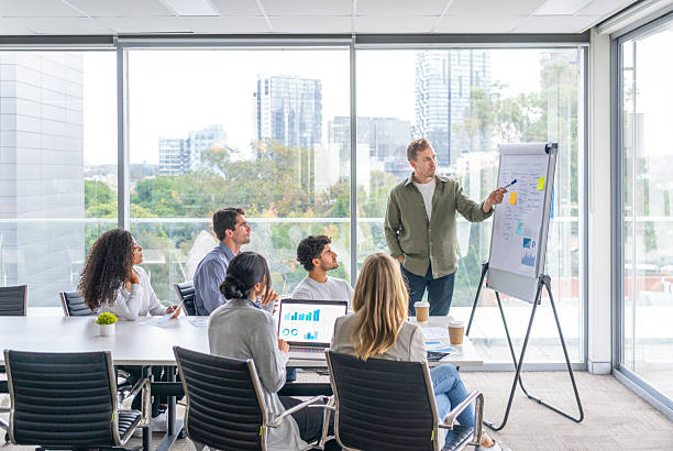 istock Business people watching a presentation on the whiteboard. A man is writing on the whiteboard with charts and graphs. 2229807571