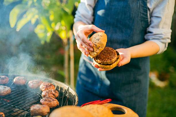 Close-up of woman preparing burgers on a BBQ grill at the front yard.