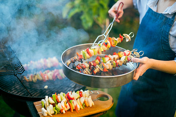 Young woman grilling delicious food on the hot smoking BBQ grill outdoors in the garden.