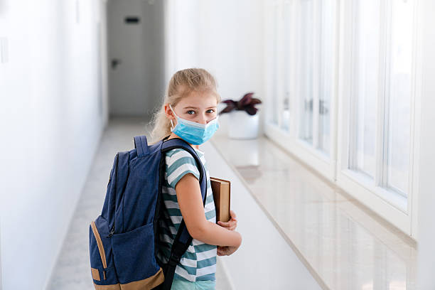 istock Kid in face mask at school inside. Back to school concept. Child with backpack and book 2229821357