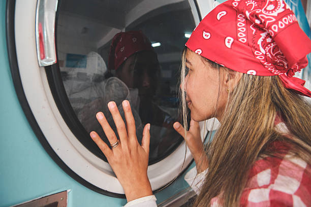 Laundromat worker wearing bandana checks progress of clothes washing inside blue washing machine