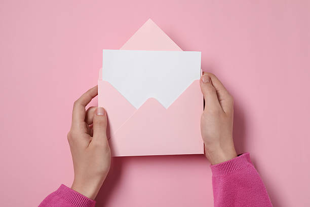 istock Woman holding letter envelope with card at pink table, top view 2229823912