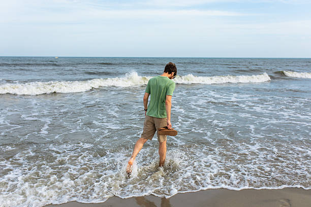 a man walking on sand in the ocean surf looking down in Ocean City, New Jersey, United States