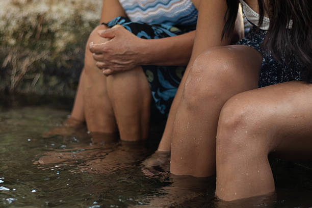 Two women are enjoying the soothing warmth of a natural hot spring, immersing their legs in the mineral-rich water for relaxation and therapy