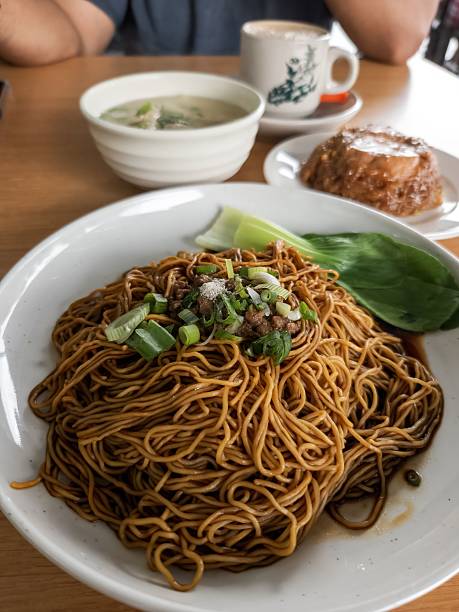 A delicious plate of noodles with soup and coffee on a wooden table at a restaurant.