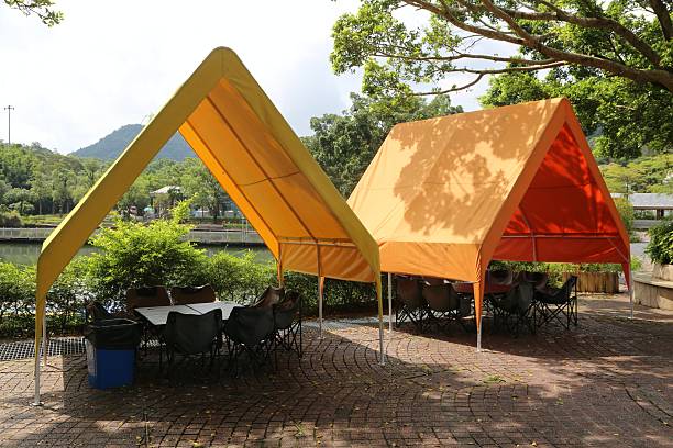 Two triangular-shaped canopy tents with gable roofs, in an orange and yellow color combination. One is a solid fabric structure, while the other has an open side panel, allowing a view of the tables inside under the canopy.
