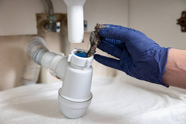 A man's hands clean the sink siphon from dirt. Water does not drain from the sink of the washbasin.