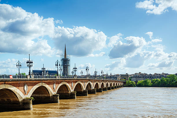A picturesque view of the Ponte de Pierre bridge spanning the Garonne River in Bordeaux, France, with beautiful historic architecture, a vibrant cityscape, and under a vibrant blue sky.