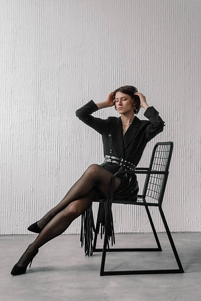 model showcases a chic black outfit while sitting gracefully on a wire chair in a contemporary studio, exuding confidence and fashion-forward vibes