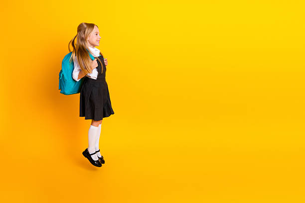 istock Smiling young schoolgirl in uniform with backpack standing on yellow background ready for a new school year 2229866390