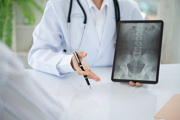 Orthopedist doctor explain spine lumber vertebrae x-ray image on digital tablet to the patient for diagnose Herniated Disc disease and Spondylosis, Spondylolisthesis. stock photo