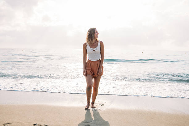 istock Woman Walking Barefoot on Sunny Beach Shore 2229879231