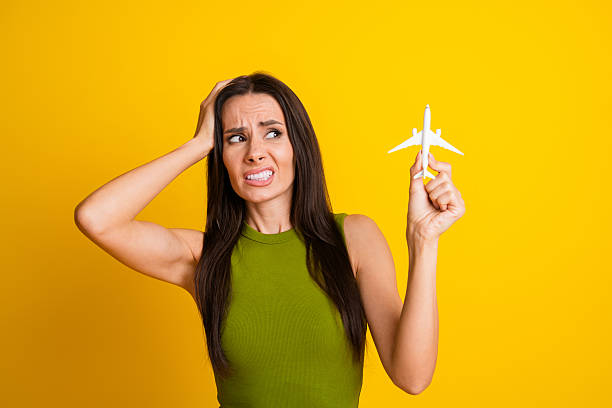 istock Young woman holding small airplane, expressing concern on bright yellow background, symbolizing travel anxiety or air travel concerns 2229880371