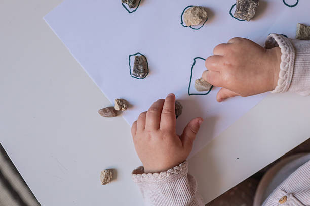 istock Toddler engaging in a rock sorting and matching activity, placing natural stones on drawn outlines. Montessori-inspired learning for sensory development and hand-eye coordination 2229880611