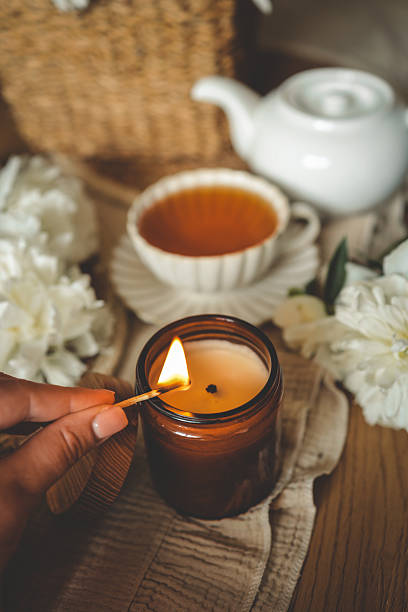 istock Hand lighting a candle in a cozy flat lay scene with tea, white peonies, straw hat, and an open book. Warm summer moment of relaxation and self-care in soft natural light 2229880883
