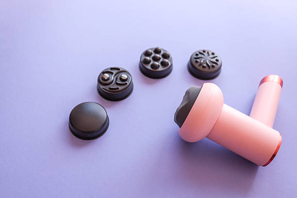 istock Pink massage gun with five black interchangeable heads arranged on purple background. Modern self-care device for muscle relaxation and therapy, displayed in flat lay style 2229882654