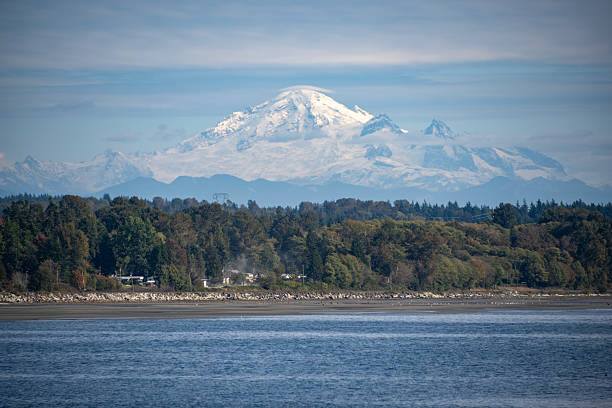 istock Snow-capped mountain looms over a serene waterfront landscape under a clear blue sky 2229883368