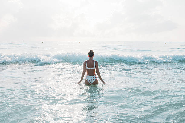 Rear view of a woman in bikini thongs looking at view during summer day from the beach. Copy space.