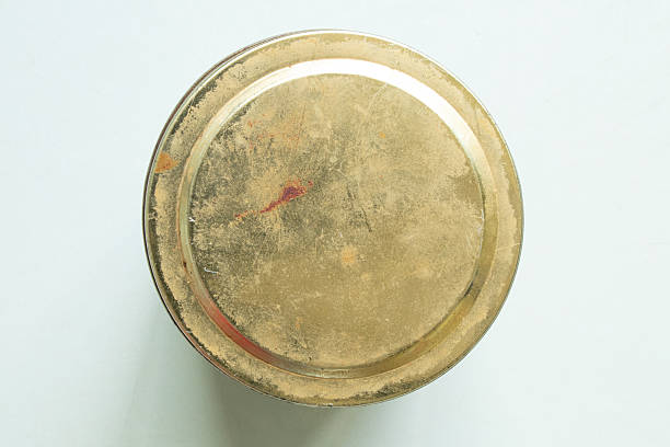Old metal jar lid with scuffs and rust on the surface, yellow, stands on the table close-up